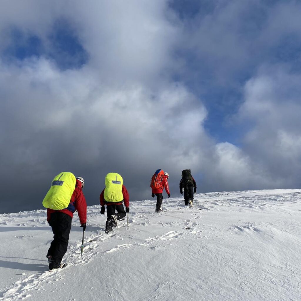 Team members walking up snow covered hill.